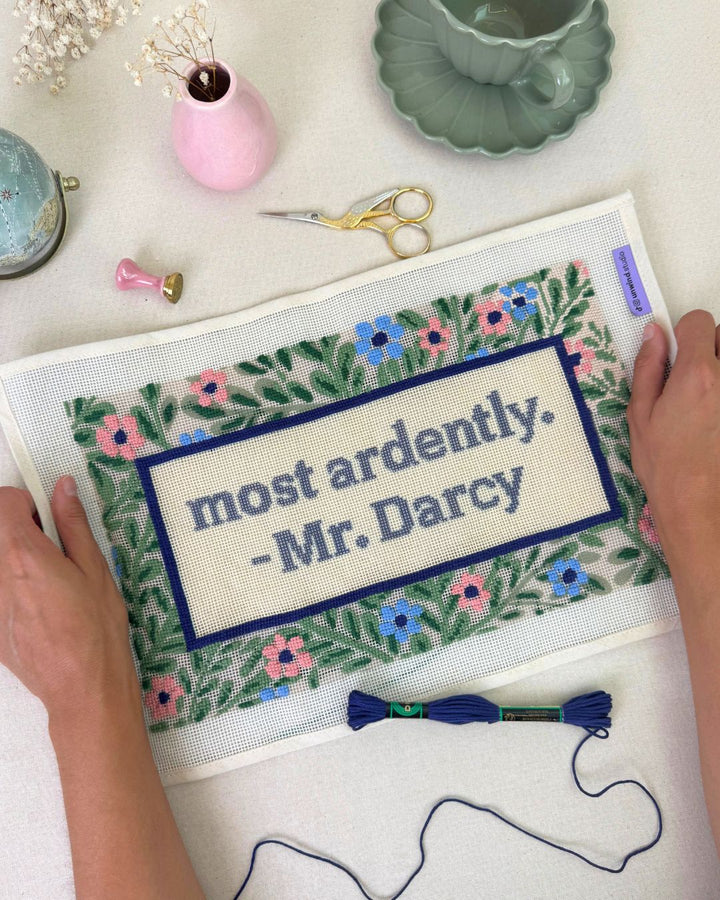 Most Ardently Needlepoint cushion canvas in progress with matching regency decor elements such as a tea cup, a letter stamp, a little globe and threads