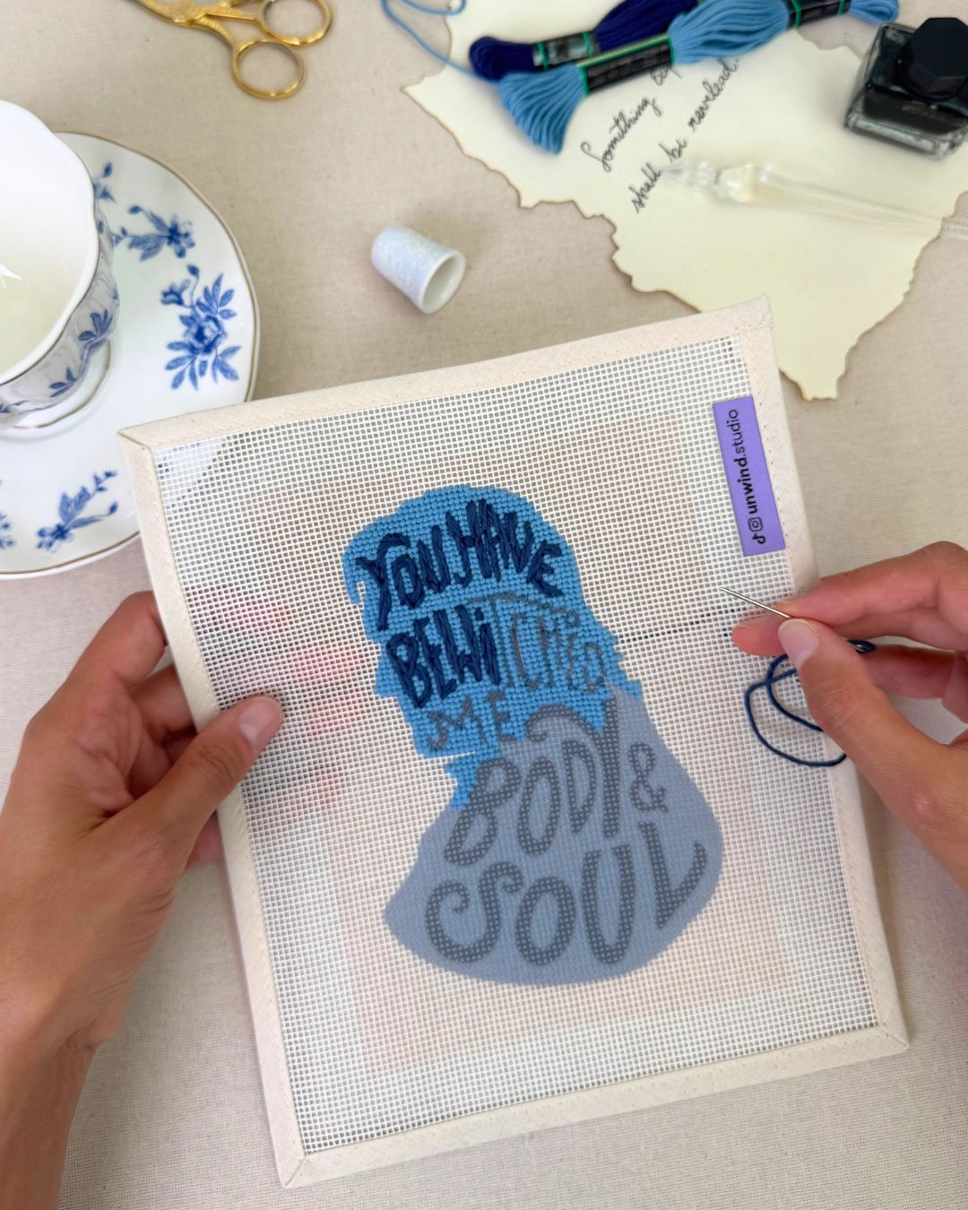 Mr. Darcy needlepoint kit with the quote "you have bewitched me, body and soul" half stitched, in blue tones with matching regency decor elements in the background
