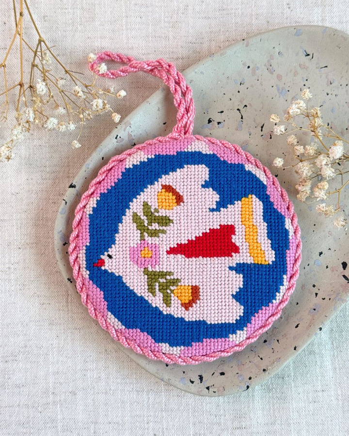 Noon folk bird ornament finished with bright and colorful tones placed on top of a ceramic plate with dried flowers next to it