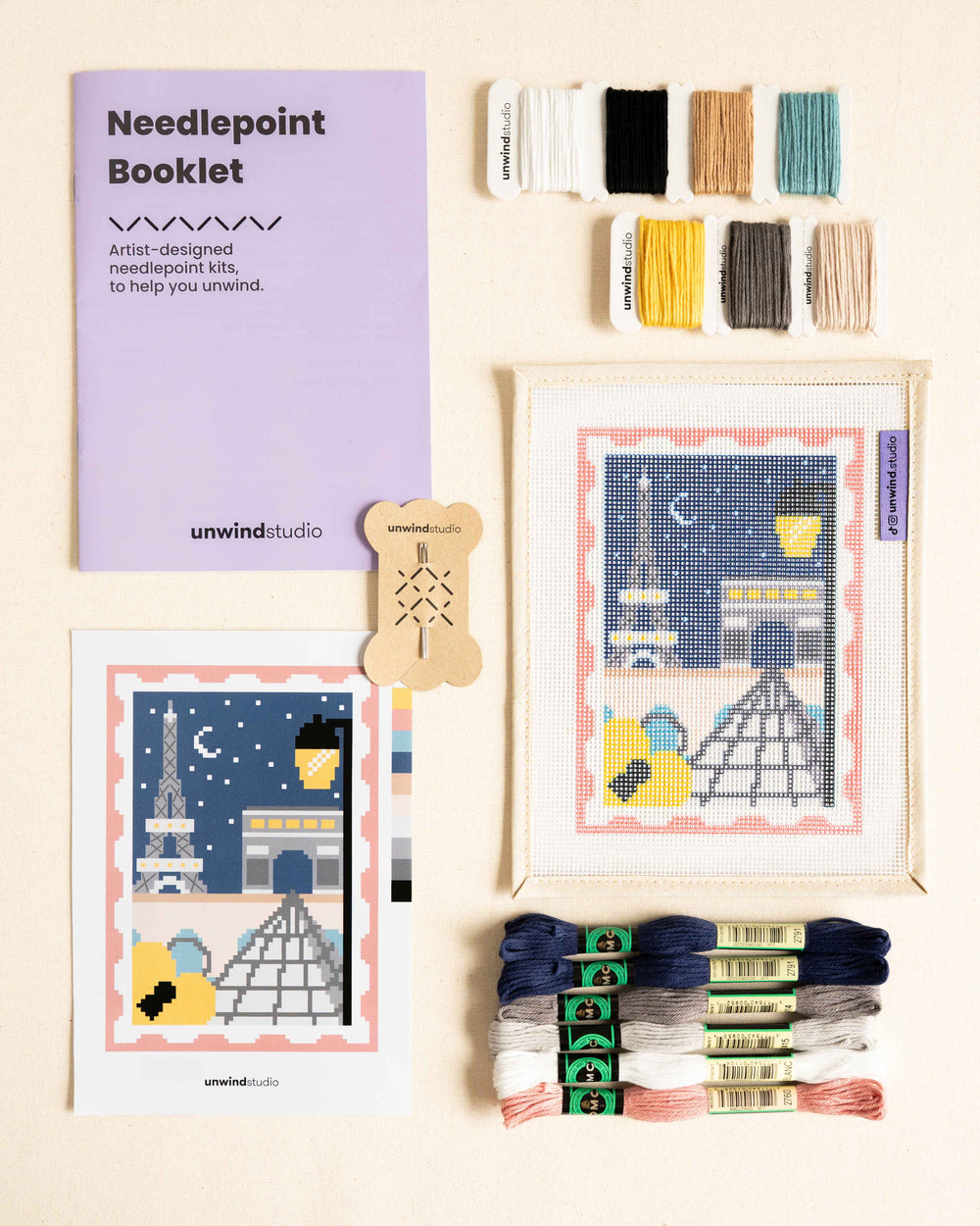 flat lay of the Paris, city of lights complete needlepoint kit with canvas, dmc soft cotton threads, grahpic flyer and needles.