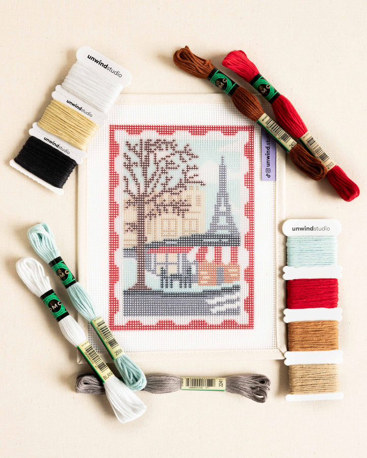 Flat lay of the Paris Stamp/Postcard needlepoint kit with matching dmc soft cotton threads