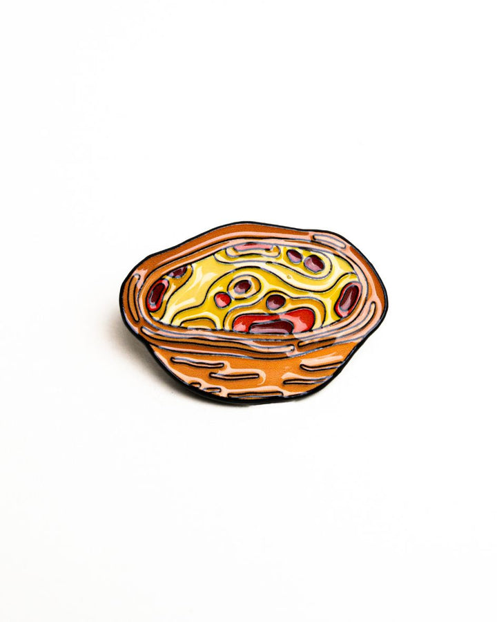 up-close shot of the unwind studio needle minder pastel de nata magnet (enamel pin) in a bold yellow and orange colors.