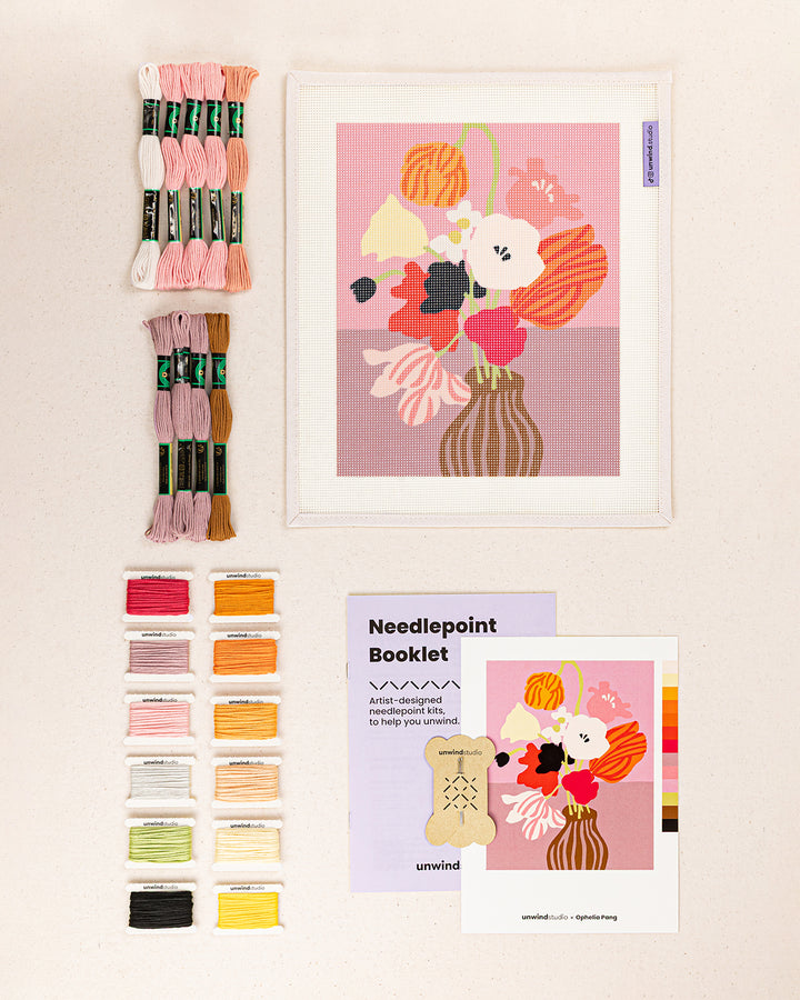 Pink Table needlepoint kit contents: printed canvas, threads, needles, and instruction booklet, graphic flyer laid flat