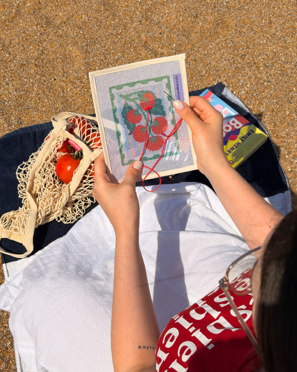 close-up shot of unwind studio pomodoro stamp needelpoint kit being stitched in a beach setting.