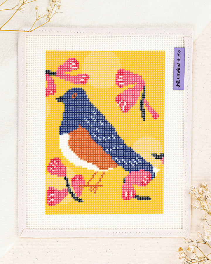 Spotted Towhee needlepoint kit by bekah worley: printed canvas of blue bird on yellow, framed with dried twigs