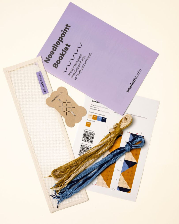 flat view of the Summit Key Fob Needlepoint Kit with blank canvas, matching threads, a instructional booklet and a graphic flyer
