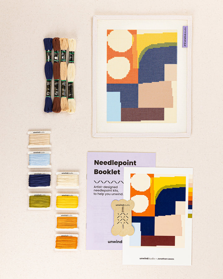 theo needlepoint kit contents: printed canvas, threads, needles, and instruction booklet, graphic flyer laid flat