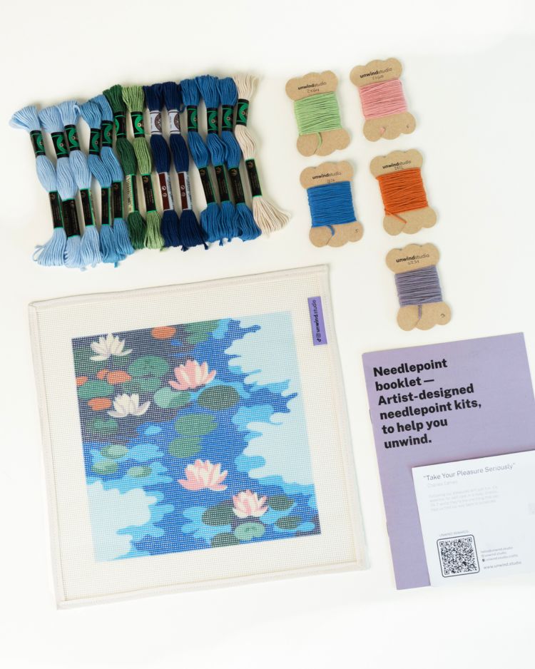 Needlepoint kit with thread skeins and a completed needlepoint piece on a white background