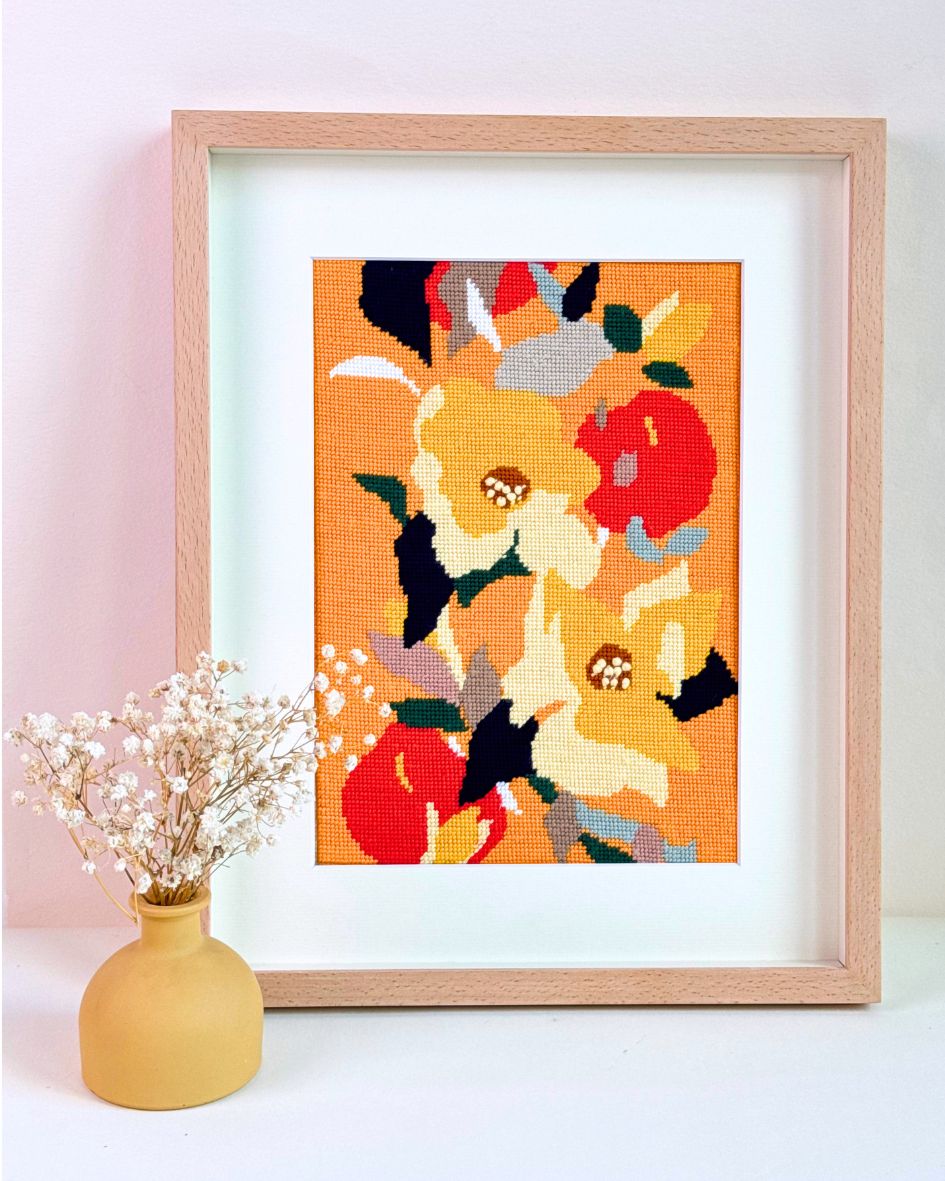 yellow delight needlepoint kit finished and framed with warm, yellow-orange tones, placed next to a yellow vase with dry flowers