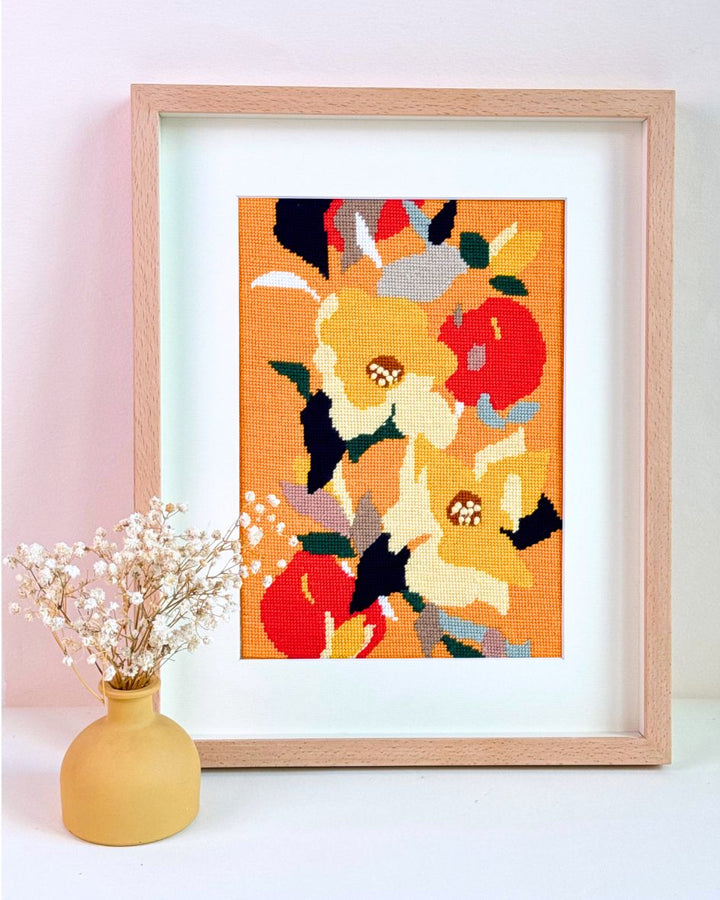 yellow delight needlepoint kit finished and framed with warm, yellow-orange tones, placed next to a yellow vase with dry flowers